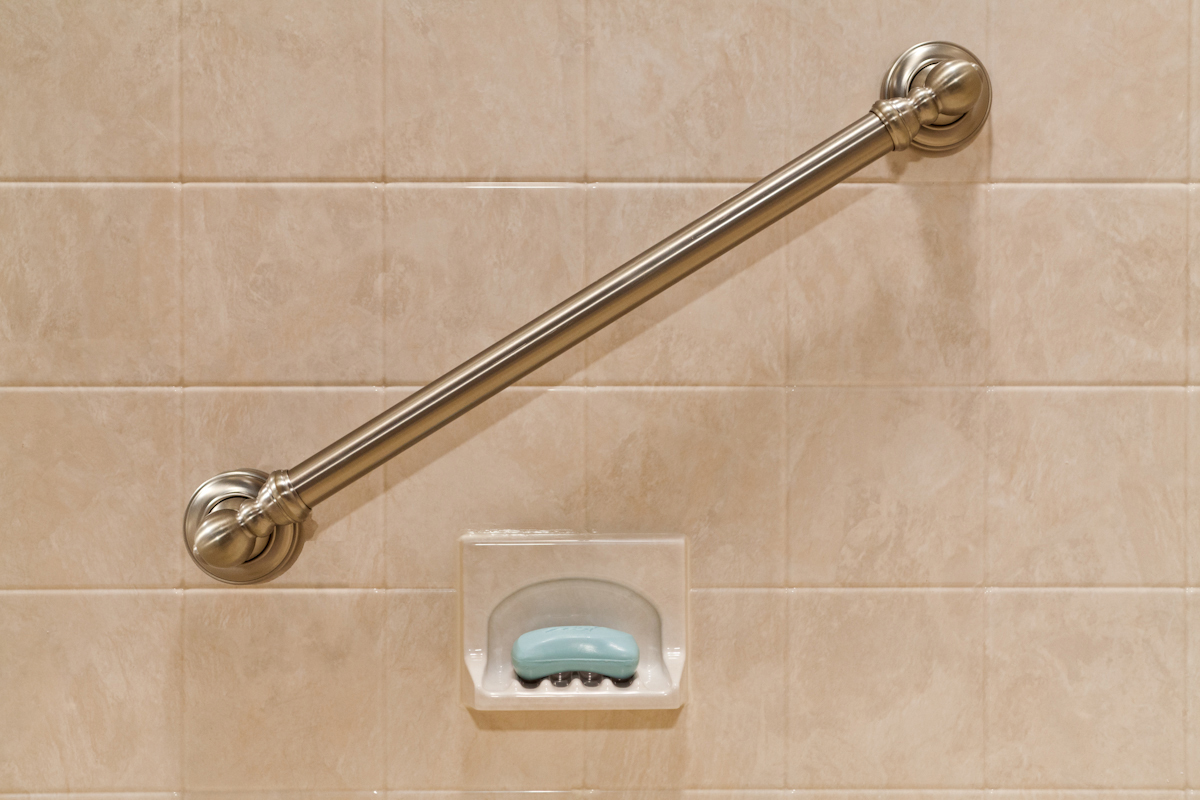 Brushed nickel angled grab bar on travertine tile