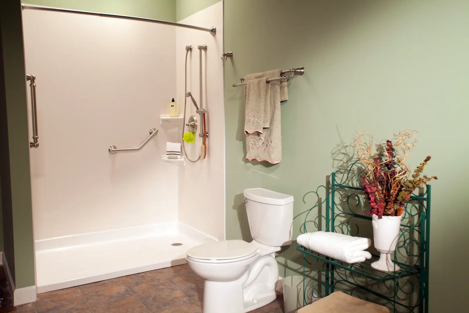 White barrier-free shower base with grab bars and handheld shower in green bathroom